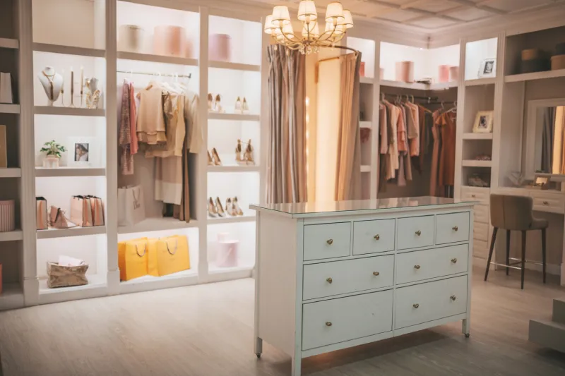 Gorgeous luxury wardrobe closet with pale pink pastel clothes on hangers and heeled shoes on shelf